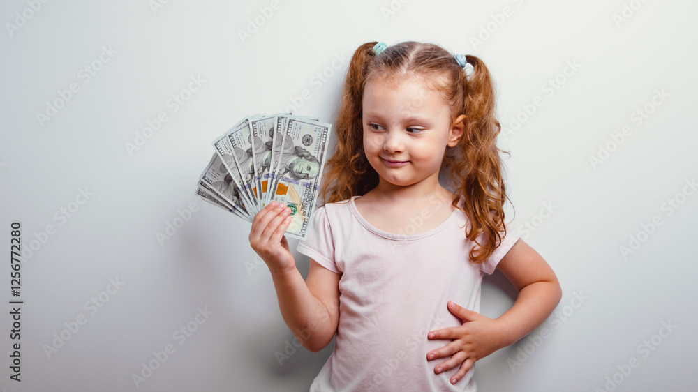 Happy thinking emotional kid girl looking on the money, cash dollars in the hand and joy on blue background. Closeup natural child