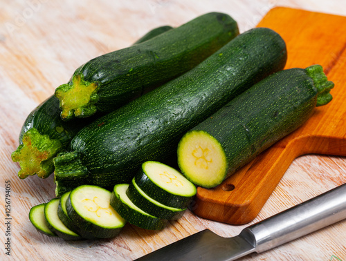 Closeup of fresh courgettes with chopped slices on wooden surface. Vegetarian food concept photo