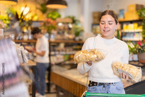 Girl compare and choosing pasta, doubt and think before buying. Client choose side dish food. Shop visitor pick up food in minimarket photo