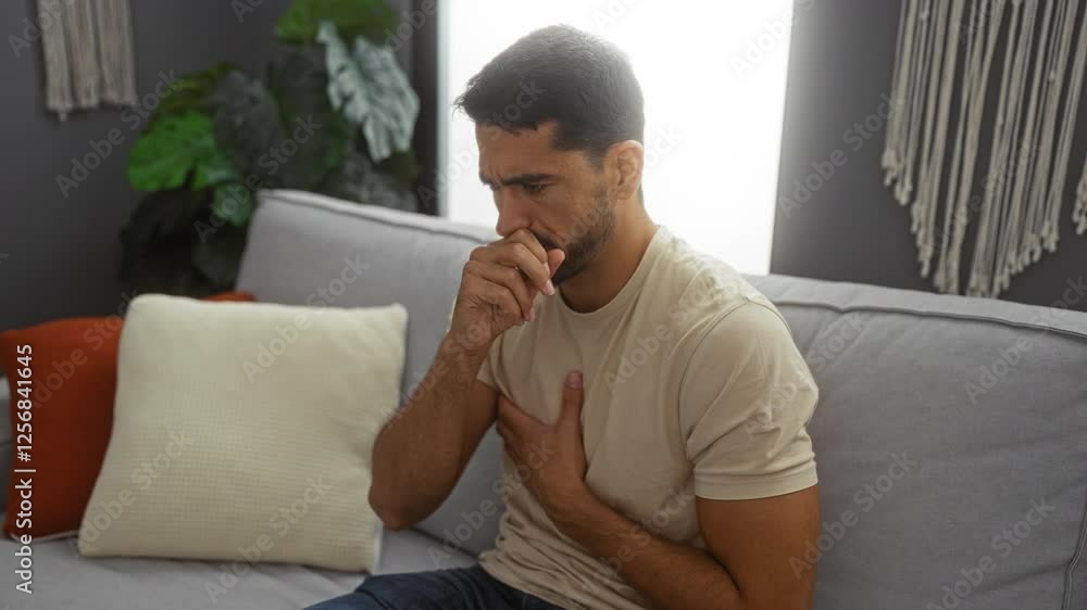 Young man indoors coughing on couch looking pensive in home setting with cozy pillows and houseplants suggesting an intimate and relaxed atmosphere Young man indoors coughing on couch looking pensive in home setting with cozy pillows and houseplants suggesting an intimate and relaxed atmosphere