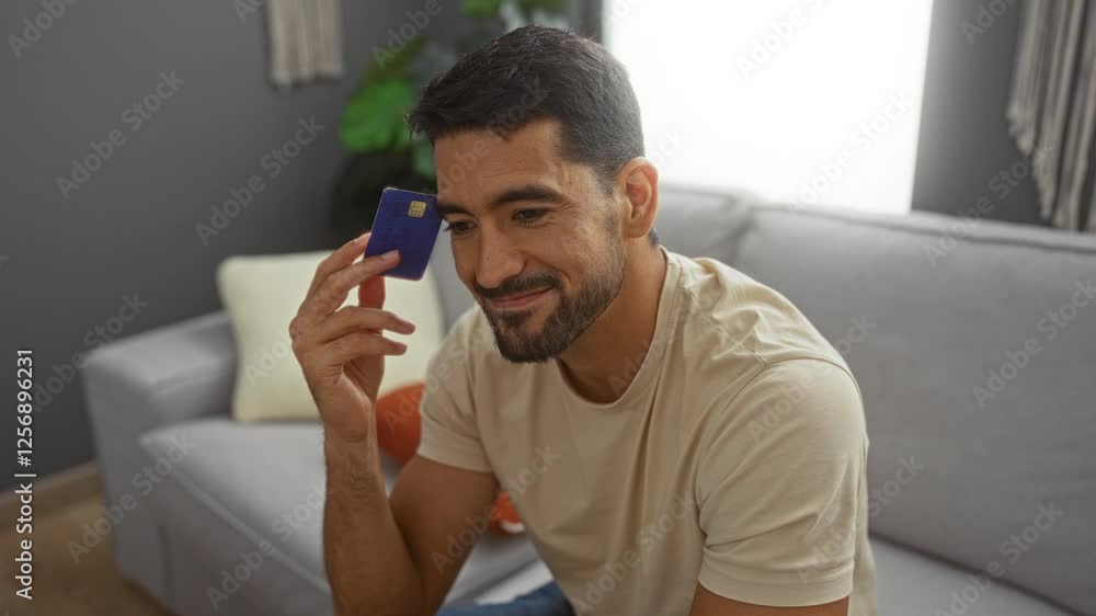 Young man with beard holding credit card while sitting on a comfortable sofa in a modern living room, surrounded by pillows and subtle greenery. Young man with beard holding credit card while sitting on a comfortable sofa in a modern living room, surrounded by pillows and subtle greenery.