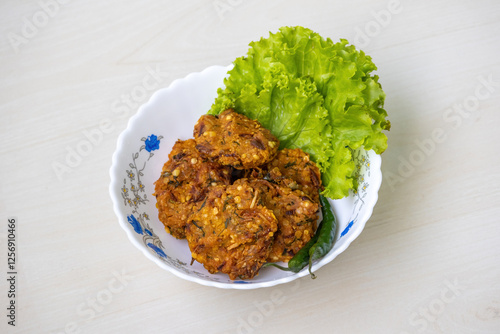 Tasty crispy fried lentil fritters called Piyaju, served in a white ceramic bowl on a light wooden surface. These onion fritters are a popular Muslim Ramadan snack. photo