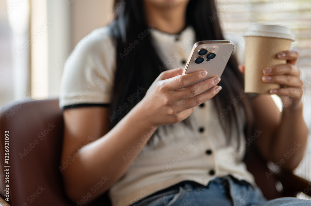 A close-up of an Asian woman's hands using her smartphone while enjoying coffee in a coffee shop. A close-up of an Asian woman's hands using her smartphone while enjoying coffee in a coffee shop.