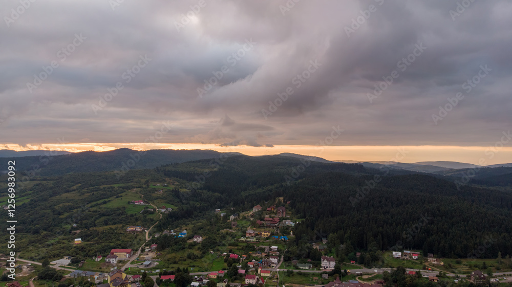 Fototapeta premium Majestic Mountains, Dense Forest, And Dramatic Clouds Illuminated By A Stunning Sunset. Aerial View Capturing The Breathtaking Beauty Of Nature From A Bird’s-Eye Perspective.
