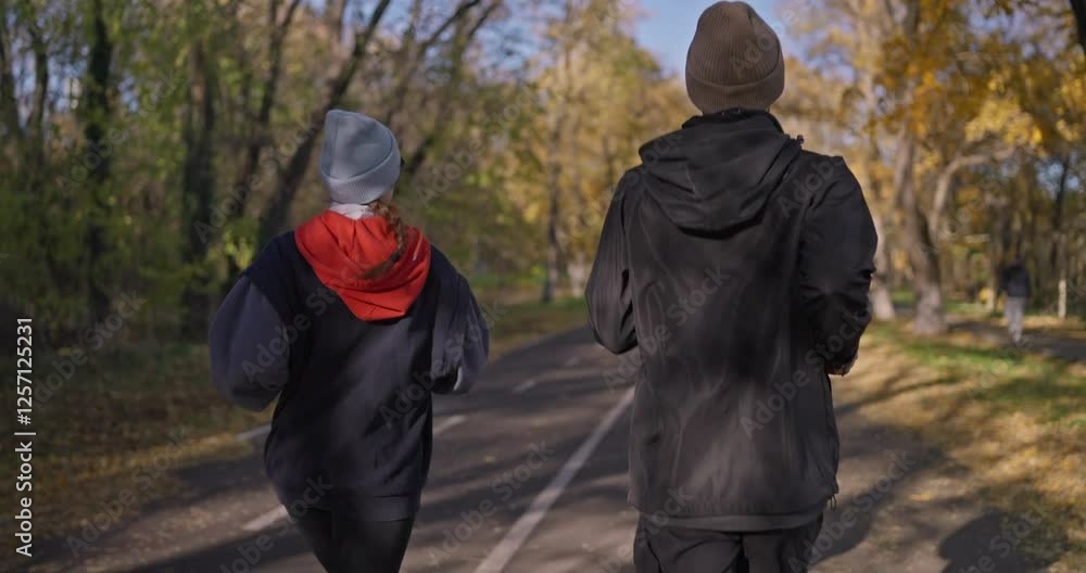 A duo a guy and a girl in sportswear are running along an alley along yellow trees in autumn in the park A duo a guy and a girl in sportswear are running along an alley along yellow trees in autumn in the park