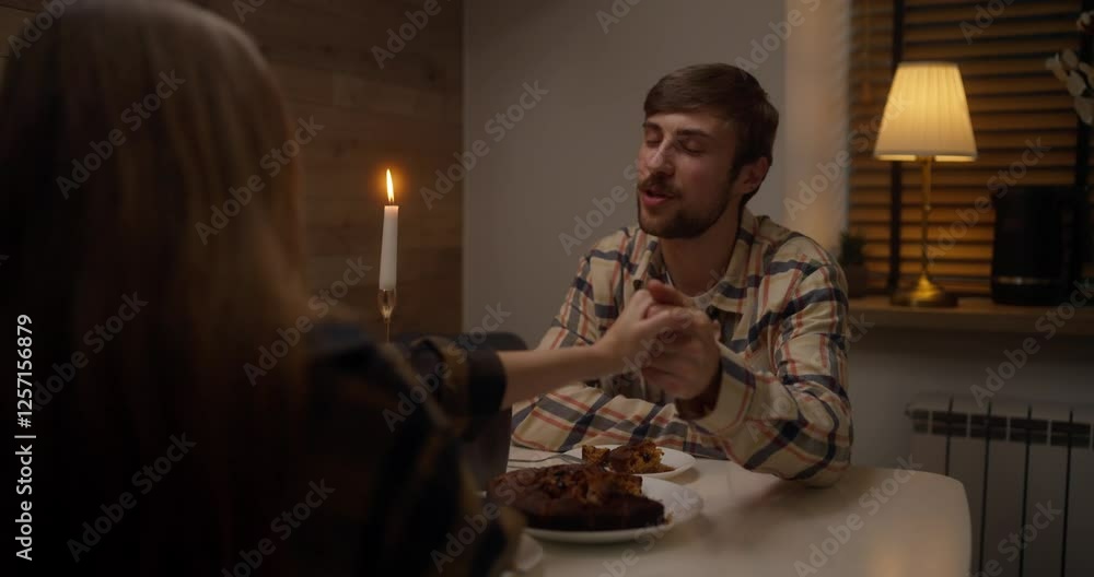 Over the shoulder a happy blond guy with a mustache and beard takes his girlfriend by the hand and communicates with her during a romantic and touching tea party in the kitchen at home Over the shoulder a happy blond guy with a mustache and beard takes his girlfriend by the hand and communicates with her during a romantic and touching tea party in the kitchen at home