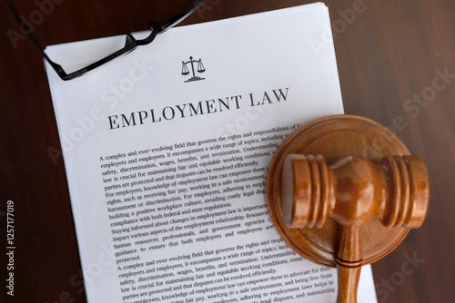 A professional setup featuring an employment law document, a judge's hammer, and glasses on an office table, representing employee rights and labor regulations.