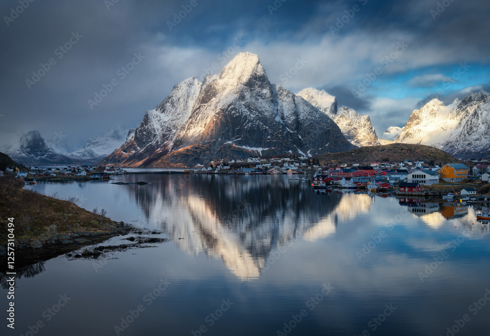 Naklejka premium Snowy mountains reflect in fjord under dramatic clouds at sunset
