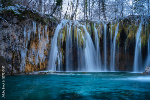 Winter waterfall, lake, frozen trees with icicles in cold evening