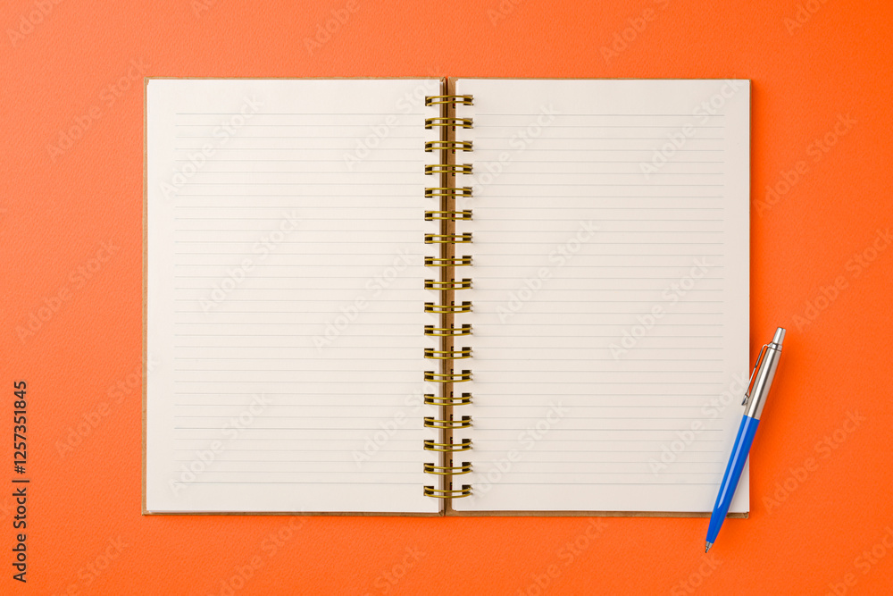 Top view of notebook and ballpoint pen on orange background Top view of notebook and ballpoint pen on orange background