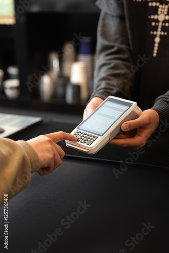 Customer's hand entering PIN code on a POS payment terminal held by a cashier, completing a transaction in a retail or service environment.