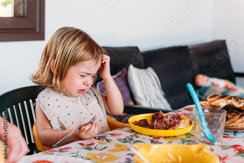 Принти на полотні Girl Expresses Sadness While Sitting at a Table With Food on Her Plate During Me