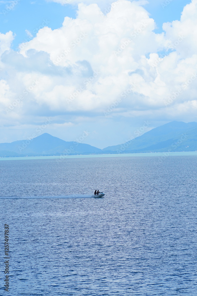 Serene tropical seascape with mountains under a bright blue sky and fluffy white clouds Serene tropical seascape with mountains under a bright blue sky and fluffy white clouds