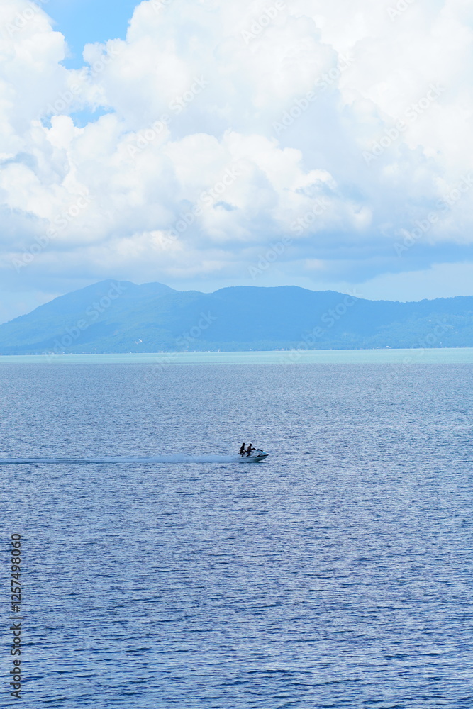 Fototapeta premium Serene tropical seascape with mountains under a bright blue sky and fluffy white clouds