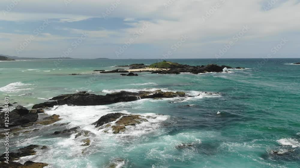 Waves crashing on rocky cliff with islet in background, Sawtell coast, Australia. Aerial backward, drone at low altitude Waves crashing on rocky cliff with islet in background, Sawtell coast, Australia. Aerial backward, drone at low altitude