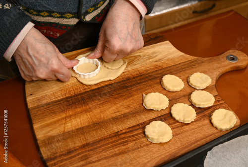 Woman prepares traditional cookies by rolling dough and cutting shapes on a wooden board