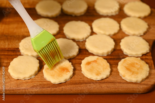 Baking cookies with a brush on a wooden board in a cozy kitchen during the afternoon