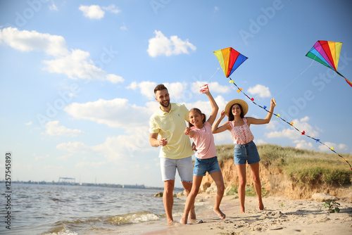 Happy parents and their child playing with kites on beach near sea. Spending time in nature
