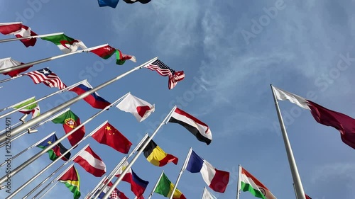 A collection of international flags waving on tall poles against a bright blue sky, symbolizing global unity and diversity.