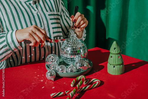 Woman cutting Christmas balls kept in plate on red table near candy cane photo