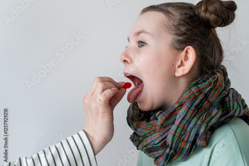 A little girl with a sore throat takes a pill. Mom's hand gives the pill to the girl. photo