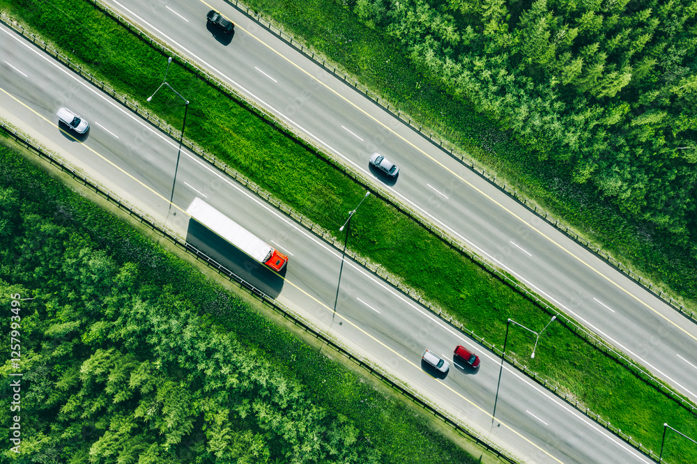 Aerial drone view of highway asphalt road with cars and trucks driving through green summer woods. Cargo delivery logistic concept