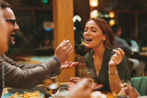 Man feeding woman delicious meal with fork while enjoying romantic dinner at restaurant