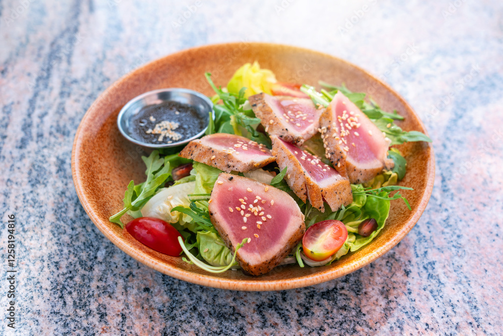 Seared sliced meat fish with mixed green fresh vegetable. Tuna Loin salad with honey orange sauce with white sesame seeds in brown ceramic plates on marble table. Seared sliced meat fish with mixed green fresh vegetable. Tuna Loin salad with honey orange sauce with white sesame seeds in brown ceramic plates on marble table.