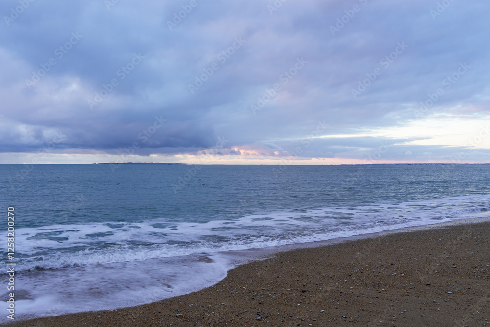 Coucher de soleil sur la Barre d’Étel sous un ciel nuageux teinté de rose. La mer calme lèche le sable doré, laissant une fine écume éphémère sur le rivage. Une atmosphère douce et apaisante. Coucher de soleil sur la Barre d’Étel sous un ciel nuageux teinté de rose. La mer calme lèche le sable doré, laissant une fine écume éphémère sur le rivage. Une atmosphère douce et apaisante.
