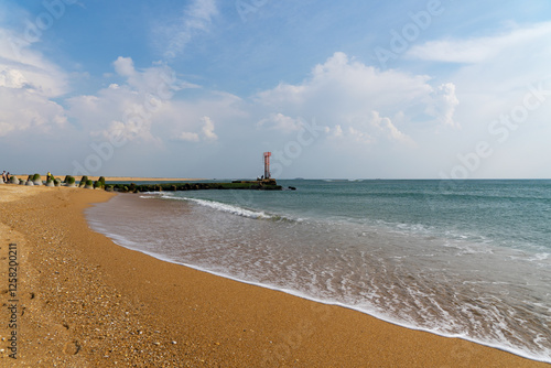 À marée basse sur la Barre d'Étel, une fine écume effleure le sable doré. Sous un ciel bleu parsemé de nuages blancs, l’horizon se fond entre mer et ciel dans une atmosphère apaisante.