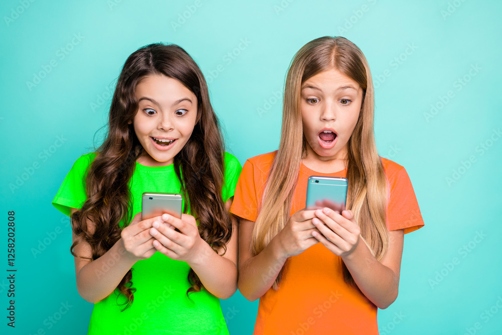 Photo of two sisters watching sales begin on their phones while isolated with teal background Photo of two sisters watching sales begin on their phones while isolated with teal background