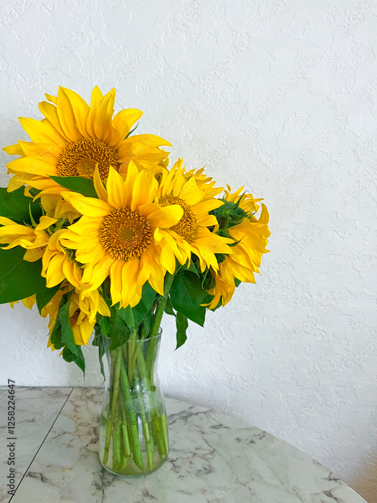 A bouquet of sunflowers stands in a glass vase on a marble table in a white kitchen