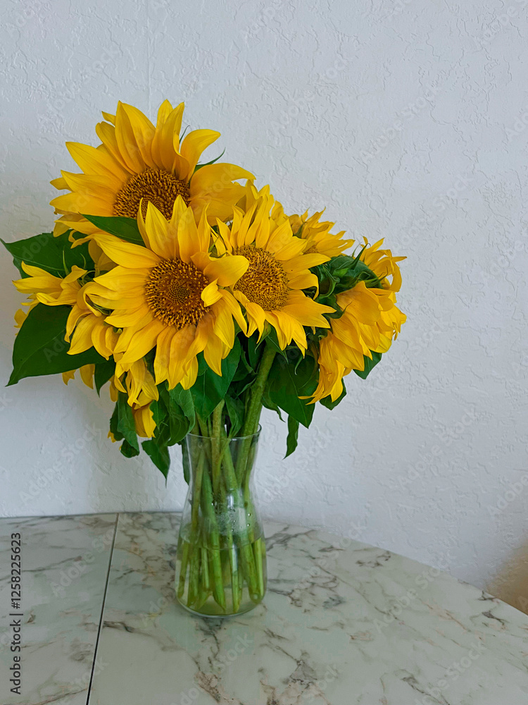 A bouquet of sunflowers stands in a glass vase on a marble table in a white kitchen