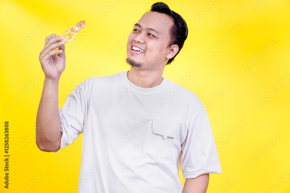 A man smiles joyfully while holding a slice of pizza against a bright yellow background. international foods day concept A man smiles joyfully while holding a slice of pizza against a bright yellow background. international foods day concept
