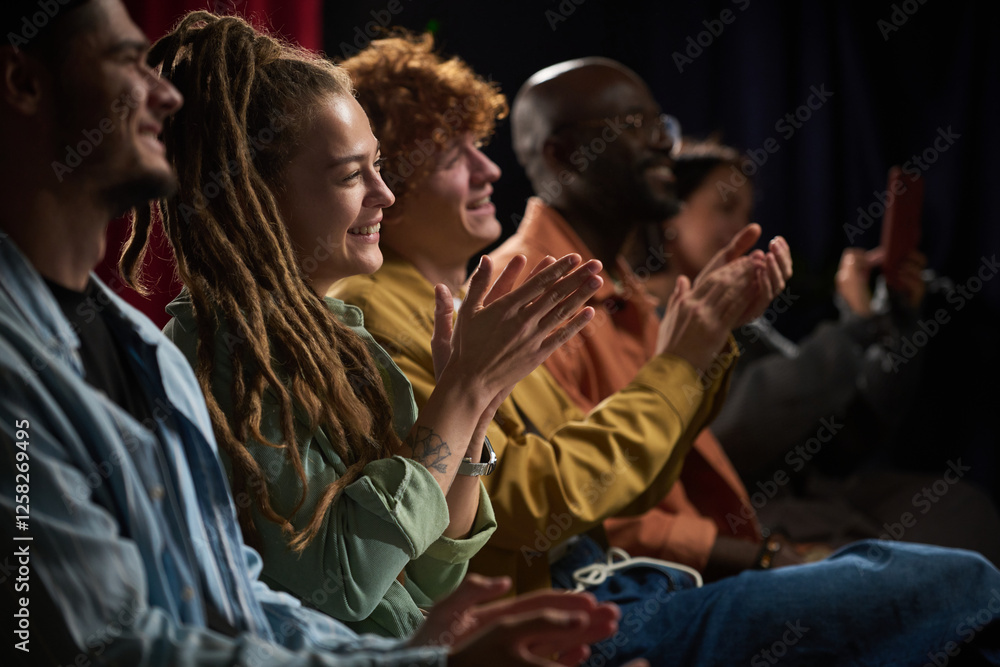 Fototapeta premium Group of diverse people sitting in row and applauding during a performance, capturing joy and engagement, showcasing various ethnic backgrounds and unity