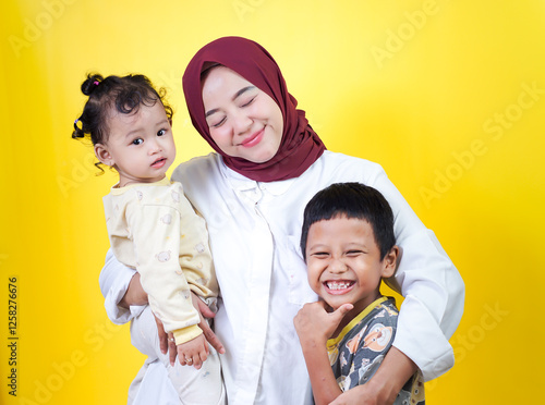 A joyful asian mother holds her two happy children against a bright yellow background. mothers day concept