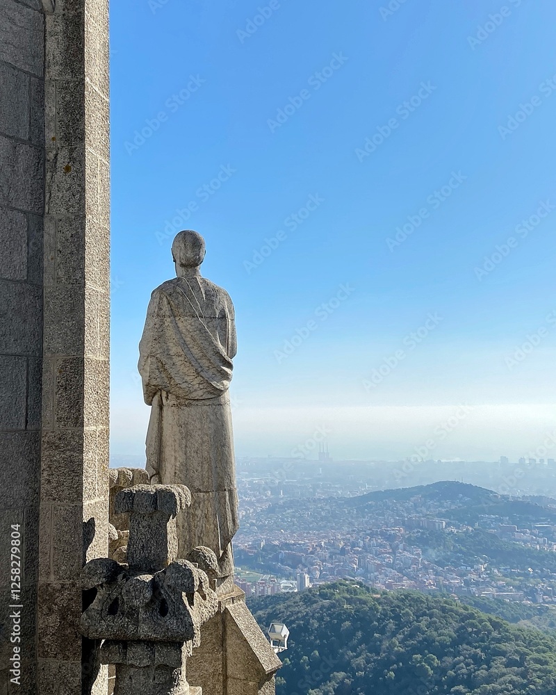 Fototapeta premium A statue stands on an outcrop in a temple, overlooking a panoramic view of a city below. The clear blue sky stretches out in the distance