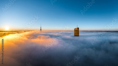 Thick fog covering Riga city in colorful sunrise colors. Drone view over old town, TV tower and river Daugava. Twilight colors in misty weather.