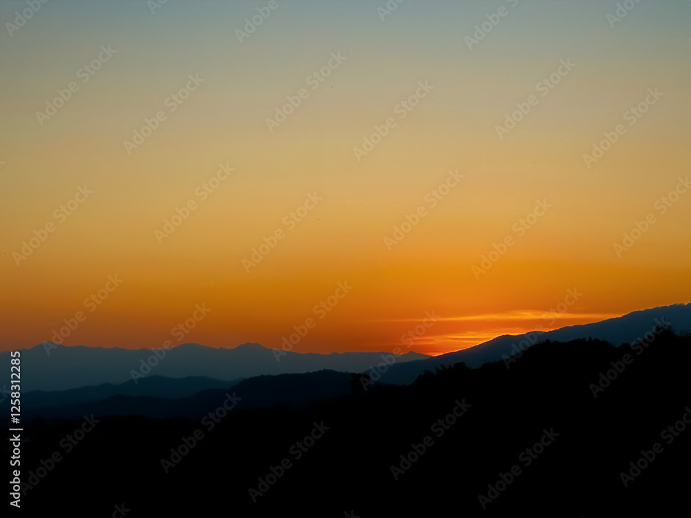 Beautiful sunset over the mountains with orange and yellow skies, silhouetting the peaks in the fading light Beautiful sunset over the mountains with orange and yellow skies, silhouetting the peaks in the fading light