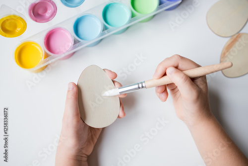 Child painting wooden egg with brush and pastel colors for Easter craft activity photo