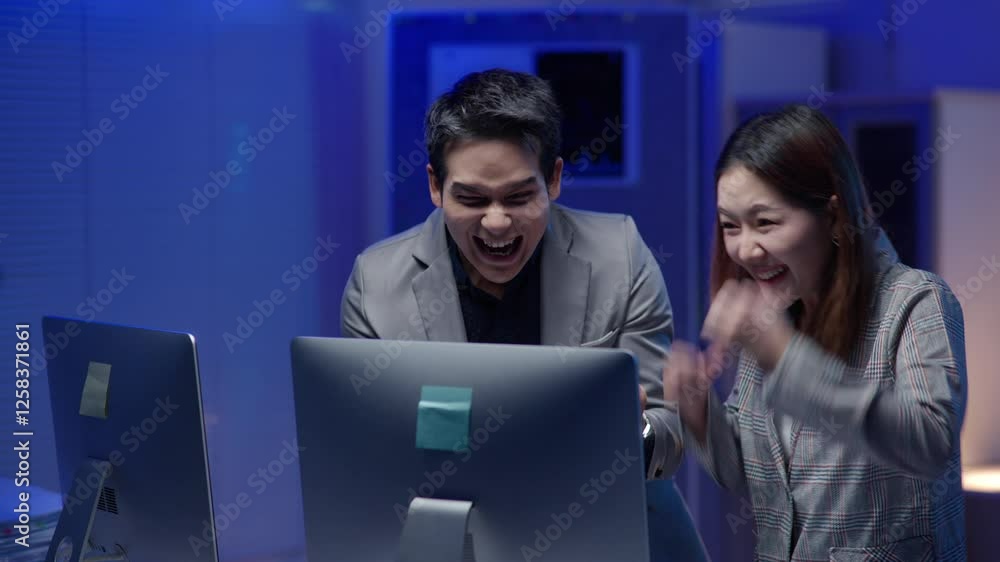 A joyful business team celebrates success in a modern office at night, with monitors displaying charts in the background. A joyful business team celebrates success in a modern office at night, with monitors displaying charts in the background.