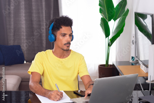 Black Man Wearing Yellow T-shirt at Remote Job in His House. He is Happy in a Teleworking Meeting at Desk With Laptop photo