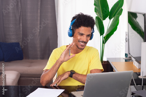 Black Man Wearing Yellow T-shirt at Remote Job in His House. He is Happy in a Teleworking Meeting at Desk With Laptop photo