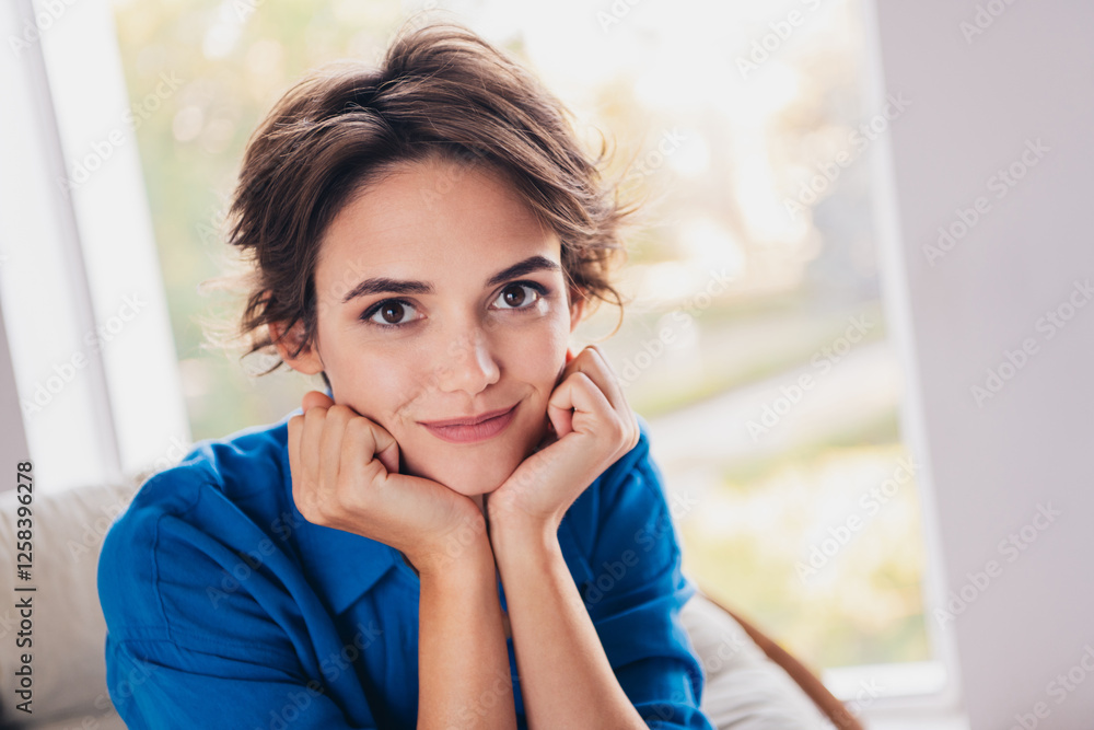 Photo of positive adorable sweet homey girl sitting with two hands under face day light indoors Photo of positive adorable sweet homey girl sitting with two hands under face day light indoors