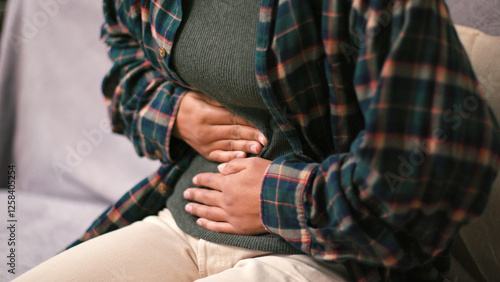 Upset Latin American woman bends massaging abdomen on sofa photo