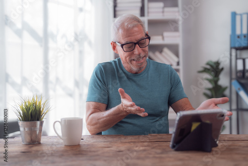 Slika na platnu Happy retired man wearing eyeglasses having a video conference using a tablet at