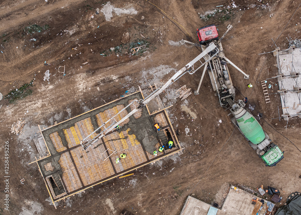 Aerial view of a construction site with workers pouring concrete using a pump truck, highlighting industrial development and teamwork in the building process. Residential construction industry.