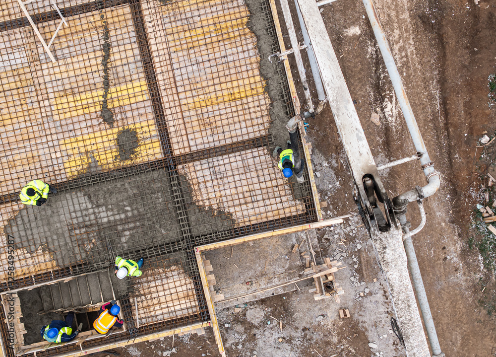 A closer aerial perspective of construction workers pouring concrete onto a reinforced foundation, showcasing precision and structural work. Residential construction industry photo.