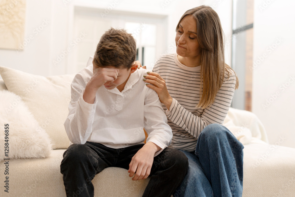 Mother comforting sad teenage son sitting on sofa at home Mother comforting sad teenage son sitting on sofa at home
