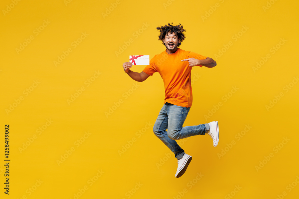 Full body young surprised happy Indian man wear orange t-shirt casual clothes jump high hold store point on gift certificate coupon voucher card isolated on plain yellow background. Lifestyle concept. Full body young surprised happy Indian man wear orange t-shirt casual clothes jump high hold store point on gift certificate coupon voucher card isolated on plain yellow background. Lifestyle concept.